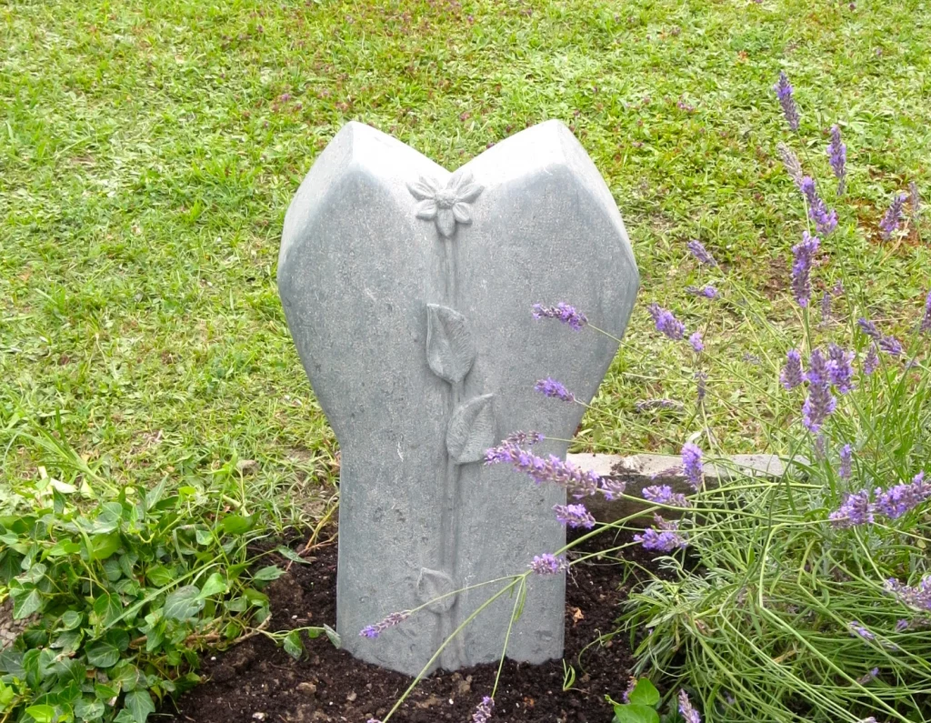 Ein Grabstein in leichter Herzform mit einem Blumenmuster darauf.
