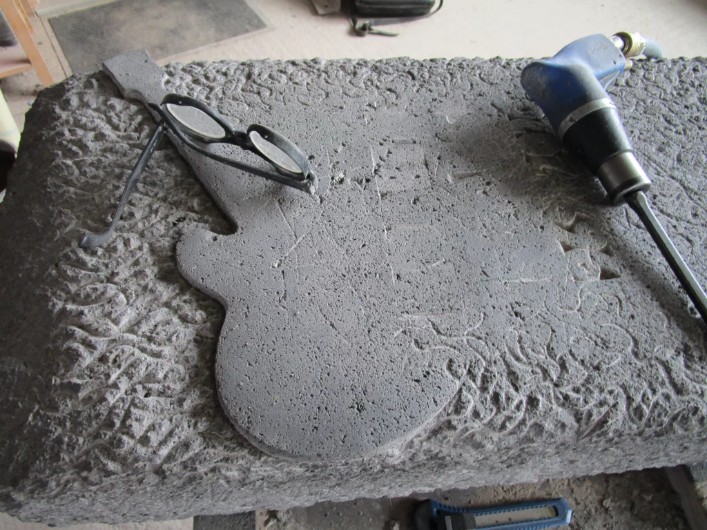 Das Motiv einer Gitarre wird in einen Grabstein in der Werkstatt gemeißelt.