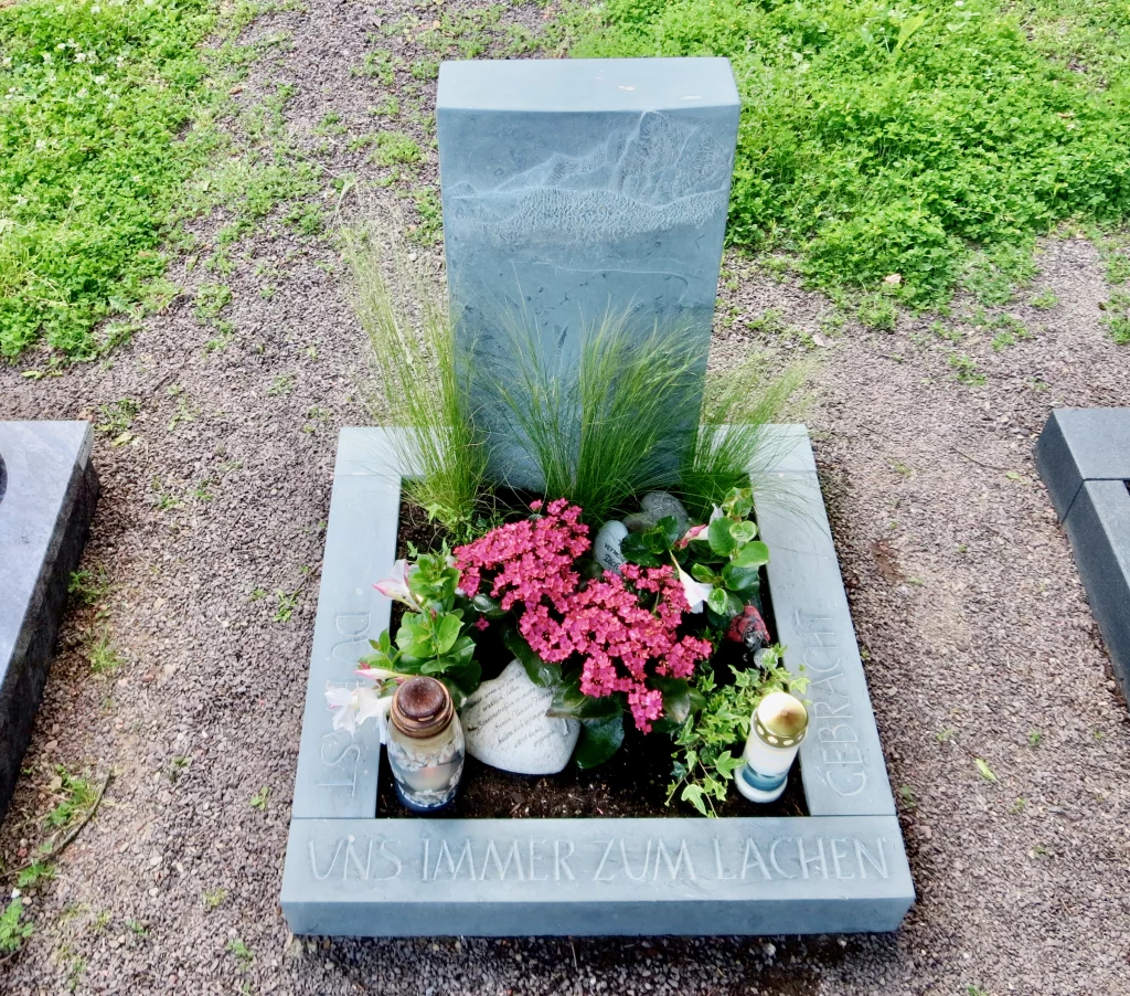 Aufnahme eines Urnengrabsteins geschmückt mit Blumen und Kerzen.