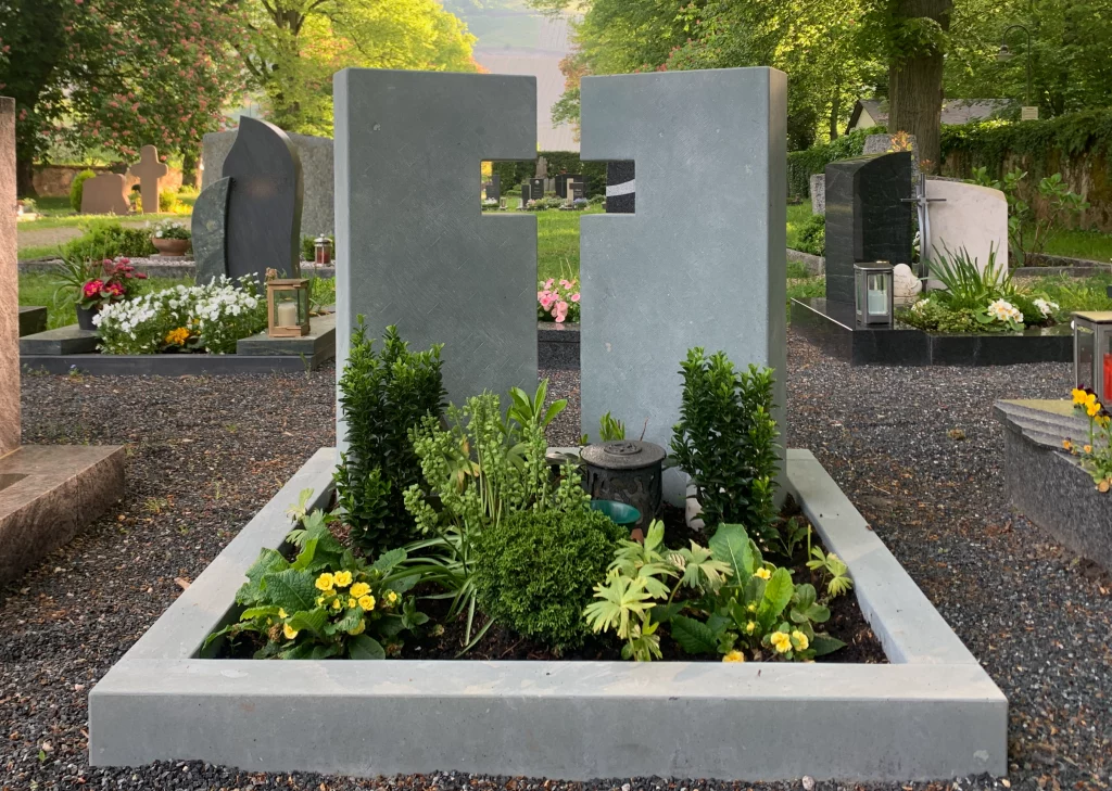 Zwei helle Urnengrabsteine deren Lücke zwischen Ihnen ein Kreuz abbildet.