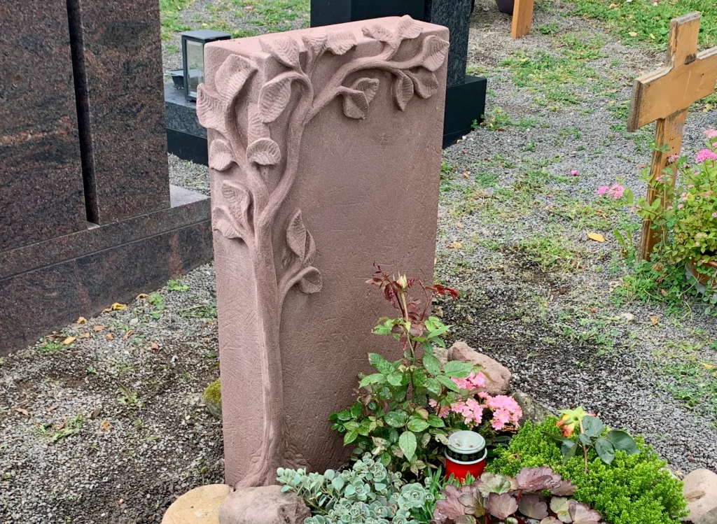 Ein rötlicher Urnengrabstein mit Ranken Motiv.