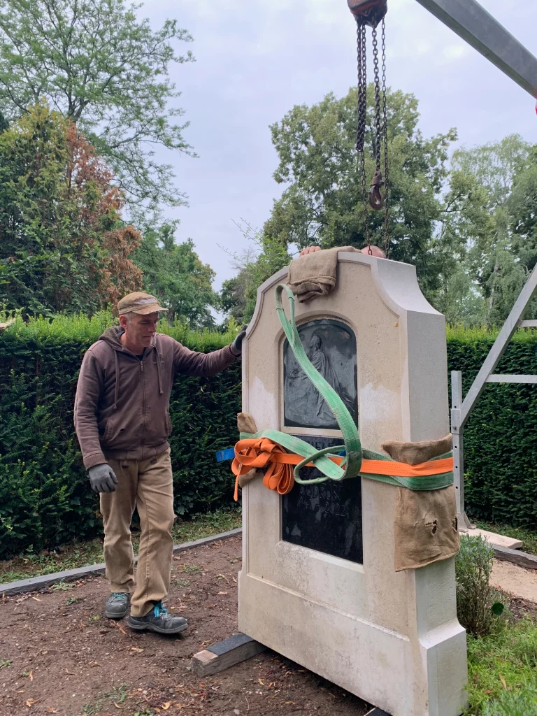 Aufnahme eines Grabsteins, der mithilfe eines Krans in korrekte Position gebracht wird.