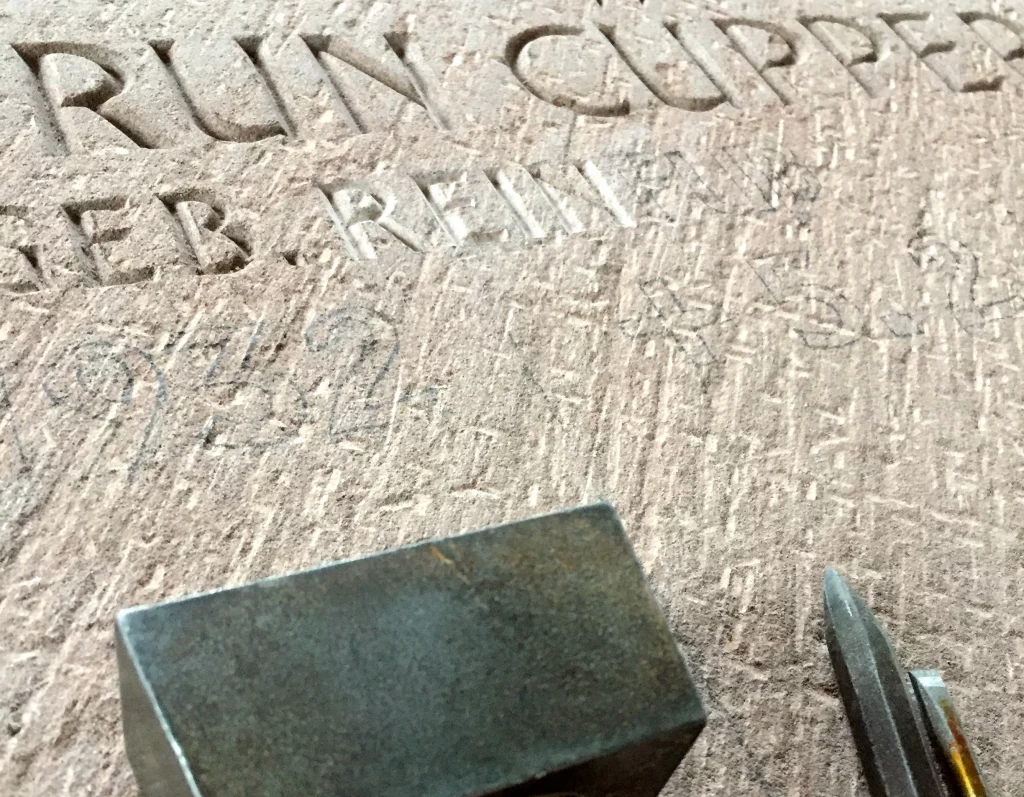 Es wird eine Detailaufnahme über den Prozess de einarbeitung der Inschrift in einen Grabstein abgebildet.